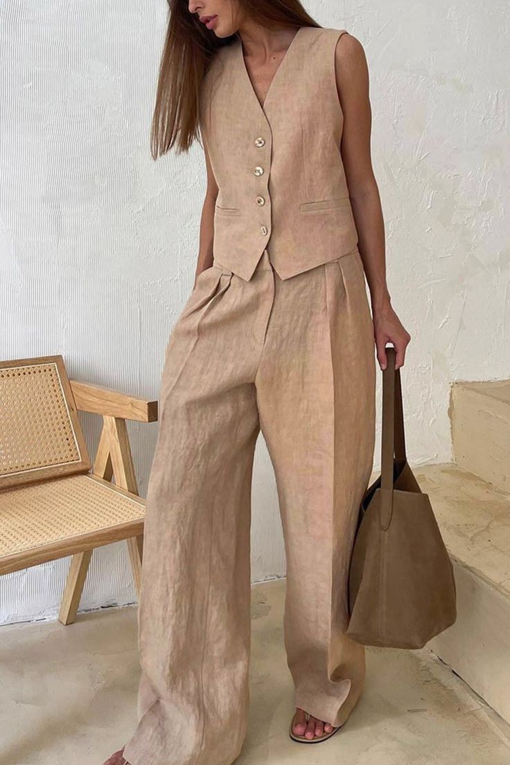 Woman in a beige linen vest and wide leg pants holding a brown bag indoors