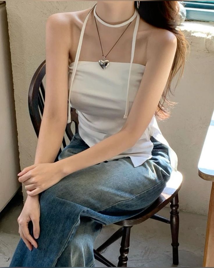 Woman in a white halter top and blue jeans sitting on a wooden chair