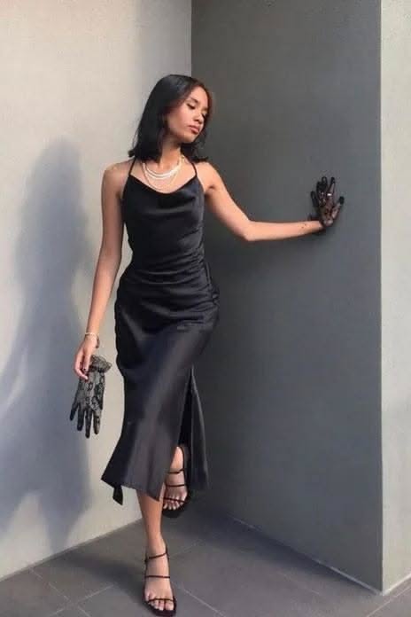 Woman in a black dress and pearl necklace posing indoors