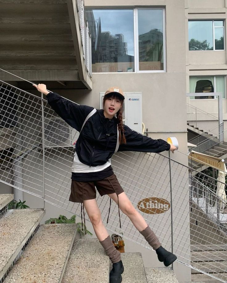 Woman with braided hair and a baseball cap posing on outdoor stairs