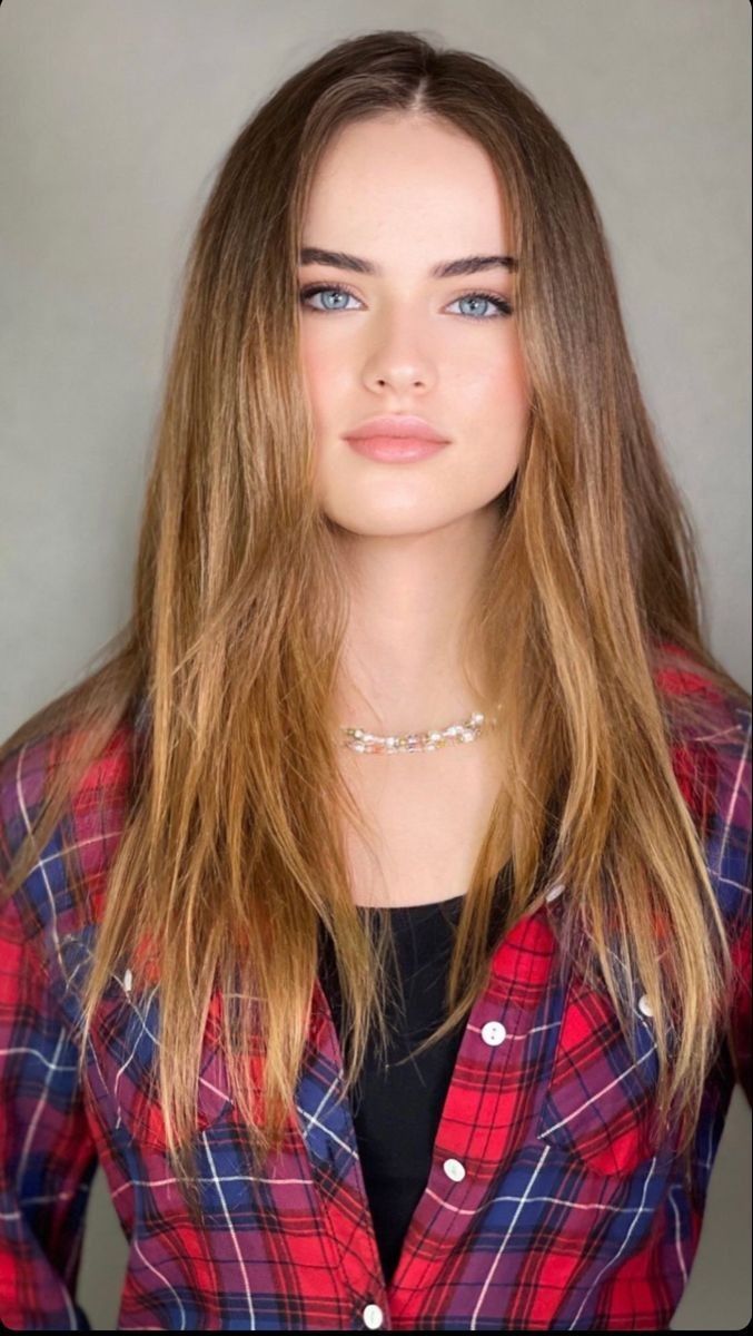 Woman with long hair and blue eyes wearing a red and blue plaid shirt