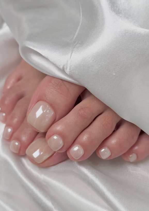 Close up of feet with a neutral-toned pedicure on white satin fabric