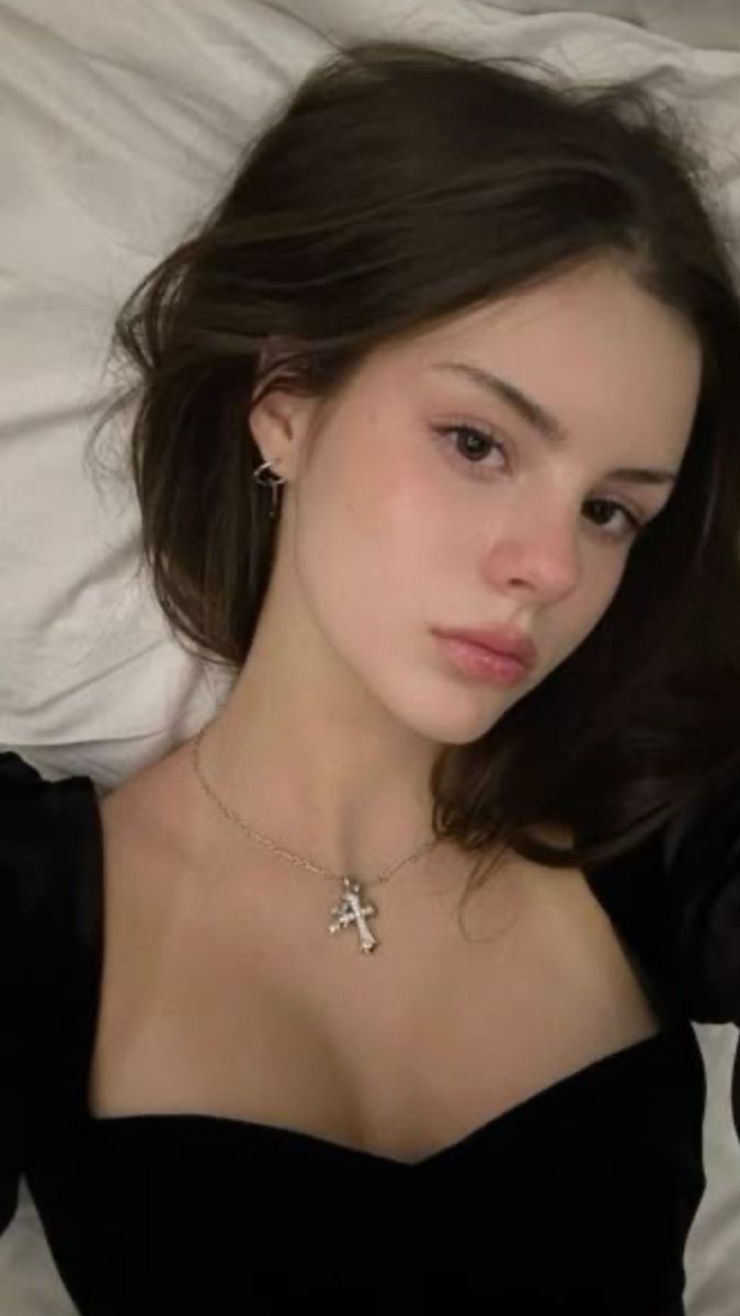 Woman with dark hair wearing a black top and silver cross necklace