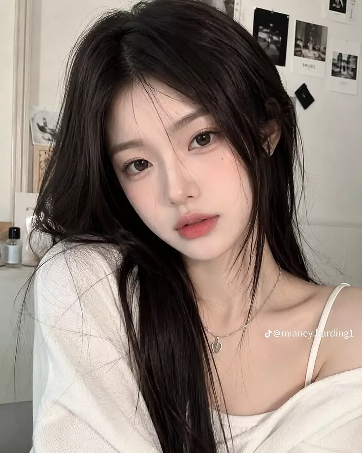 Woman with long black hair wearing a white top and silver necklace indoors