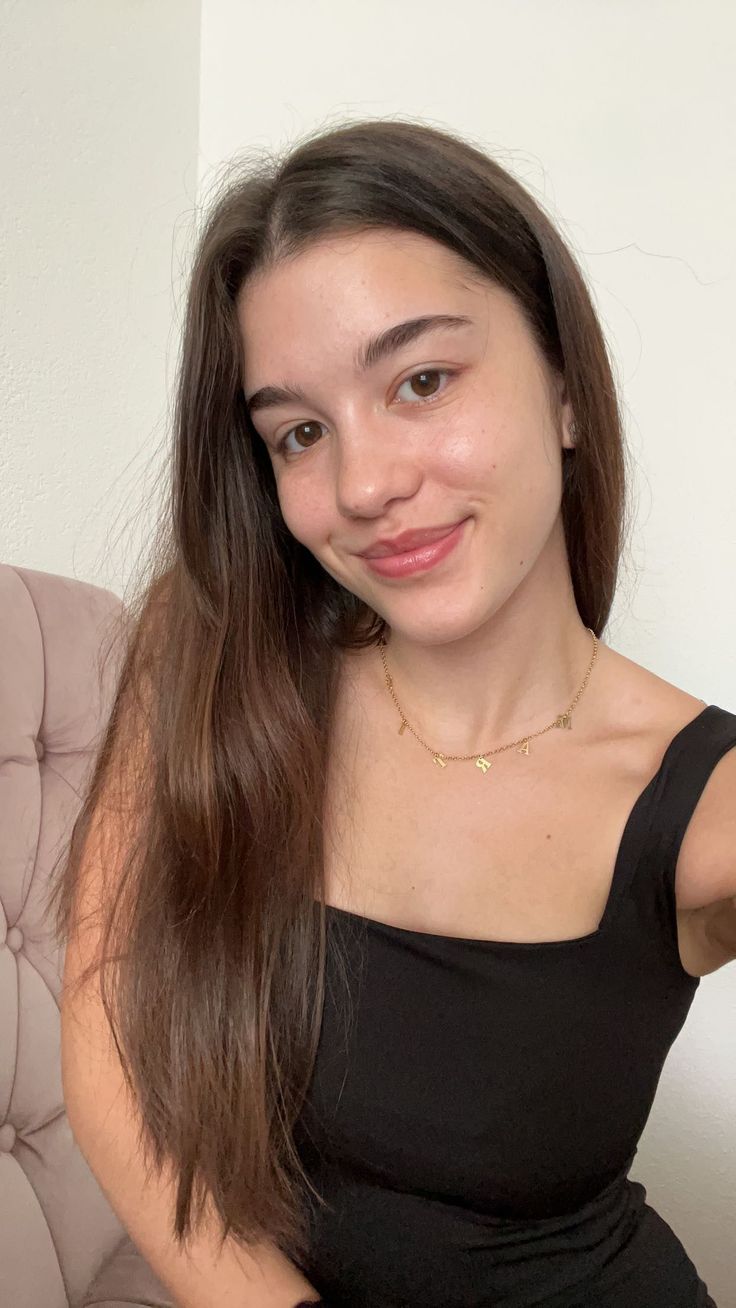 Woman with long brown hair wearing a black top and gold necklace indoors