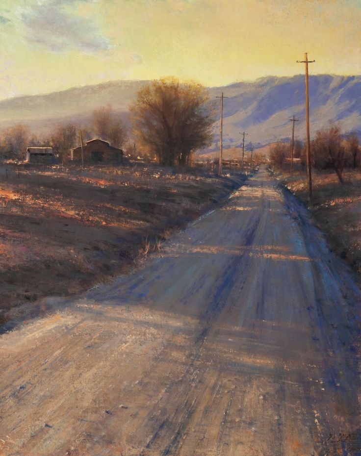 Dirt road leading to farm buildings at sunset with a mountain range in the background
