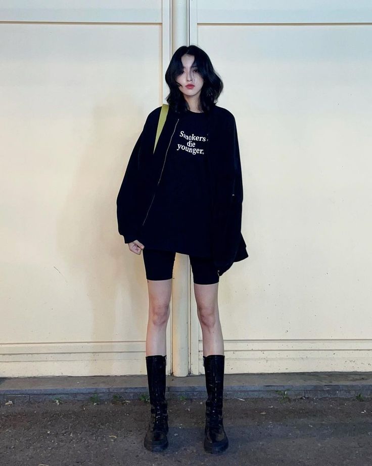 Woman with black hair wearing an oversized sweatshirt, biker shorts, and tall boots