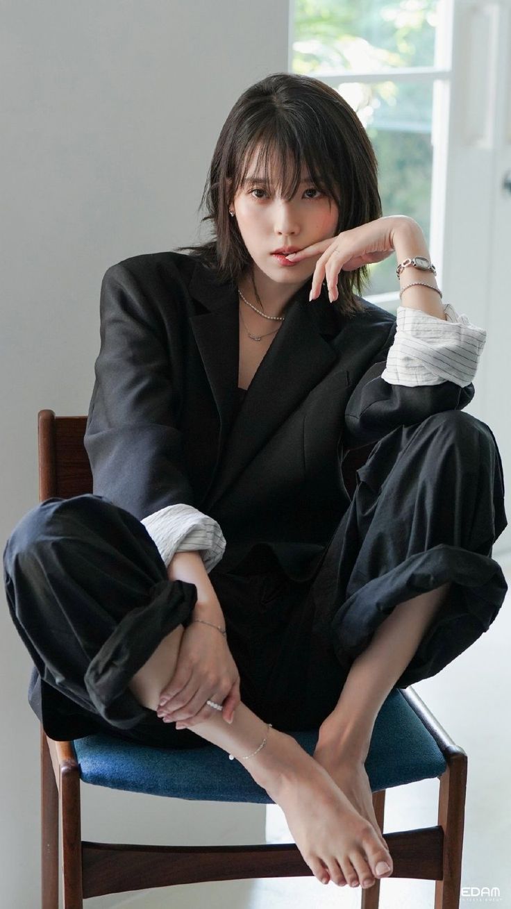 Woman in a black blazer and pants sitting on a chair with bare feet