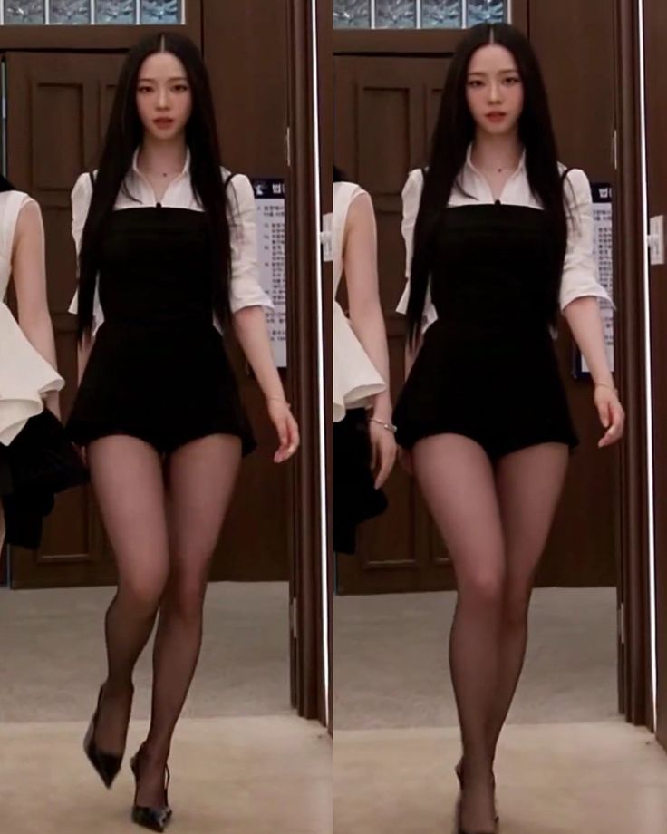 Woman with long black hair in a black dress and white shirt walking indoors