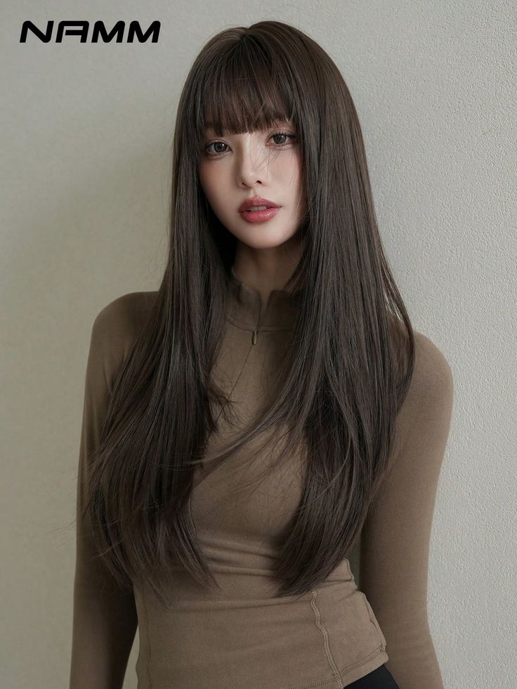 Woman with long brown hair and bangs wearing a brown long-sleeved top indoors
