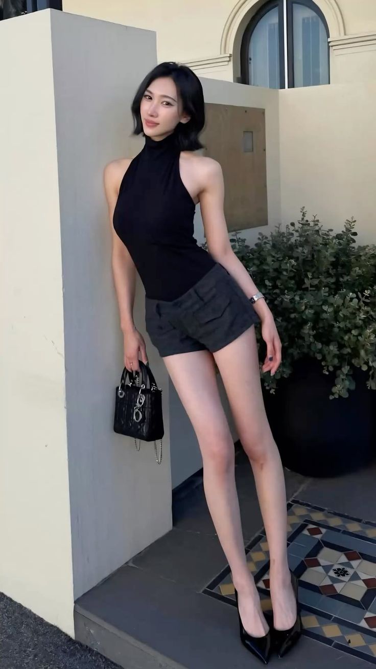 Woman in a black top and shorts posing outdoors with a handbag
