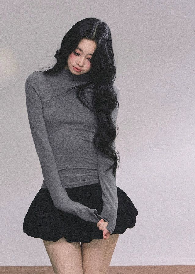 Woman with long black hair wearing a gray turtleneck and black skirt indoors