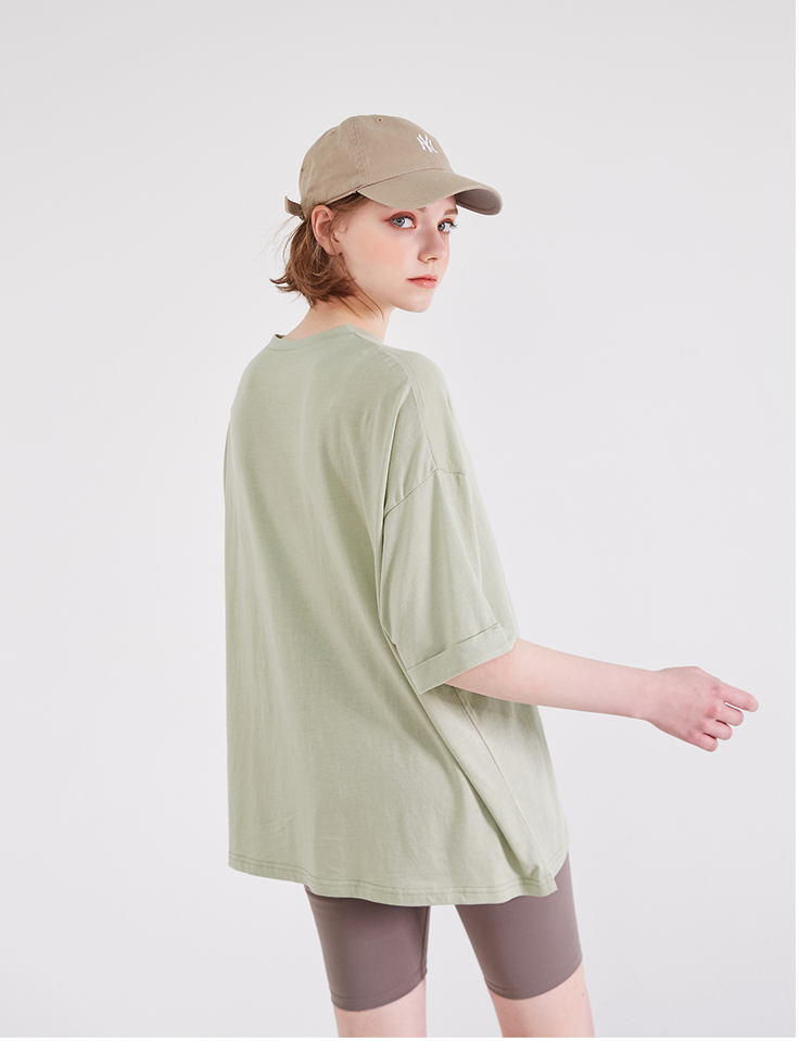 Woman in a baseball cap and oversized t-shirt looking over her shoulder