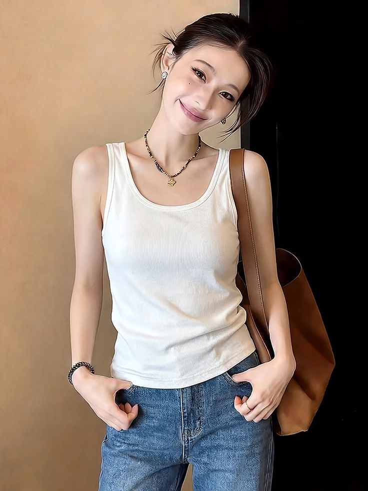 Woman in a white tank top and blue jeans with a brown bag over her shoulder