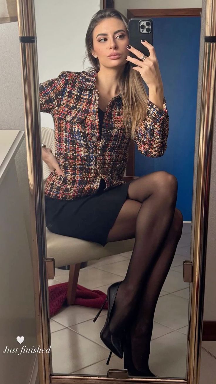 Woman in a tweed jacket and black skirt taking a mirror selfie