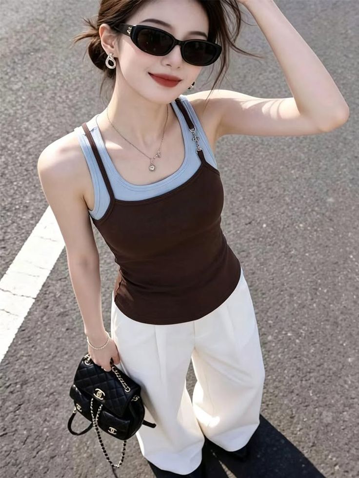 Woman in sunglasses and a tank top with white pants holding a shoulder bag