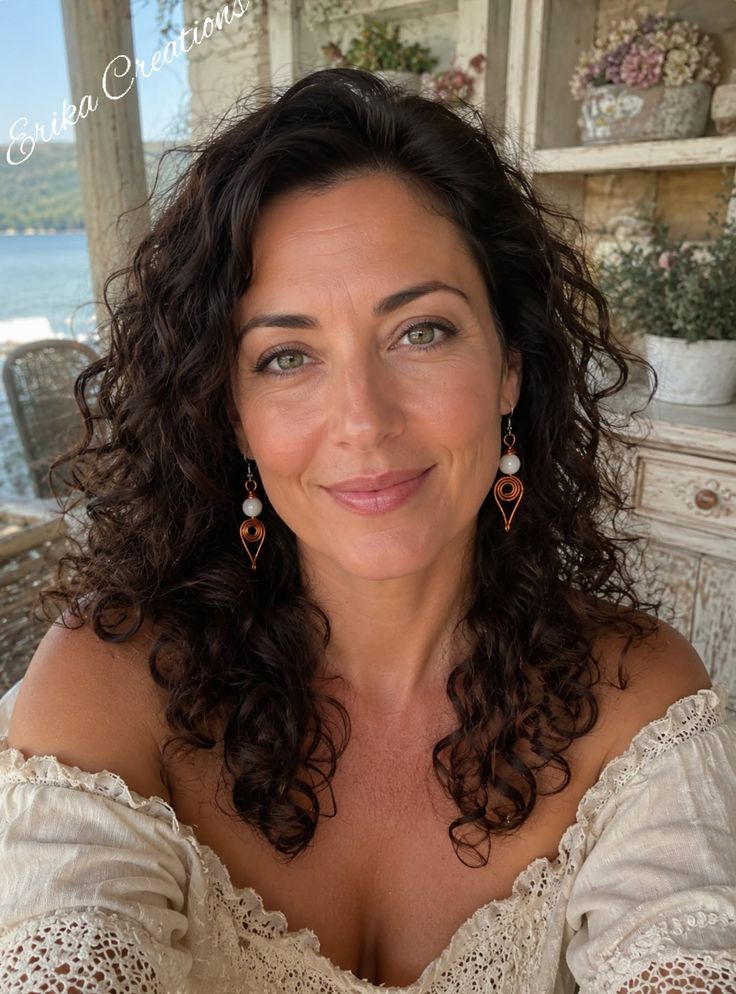 Woman with curly hair and green eyes wearing an off-shoulder top and earrings