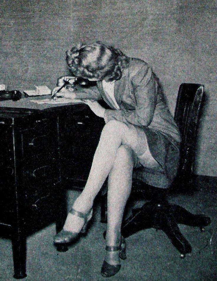 Woman in a suit jacket and stockings writing at a desk