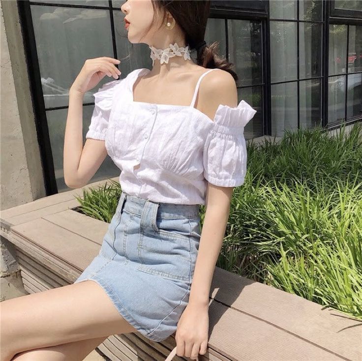 Woman in a white off-shoulder top and denim skirt sitting outdoors