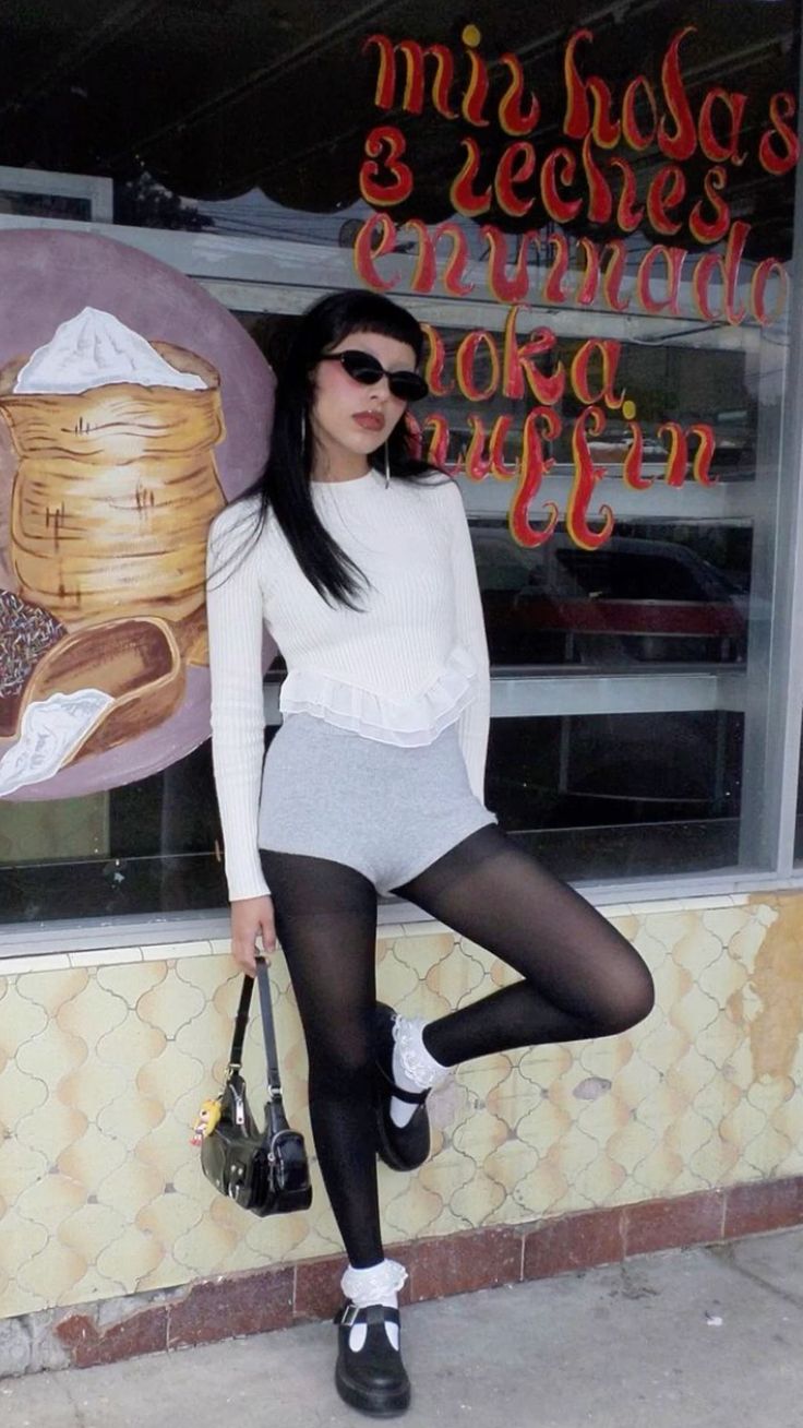 Woman with long black hair and sunglasses posing outdoors in a white top and black tights