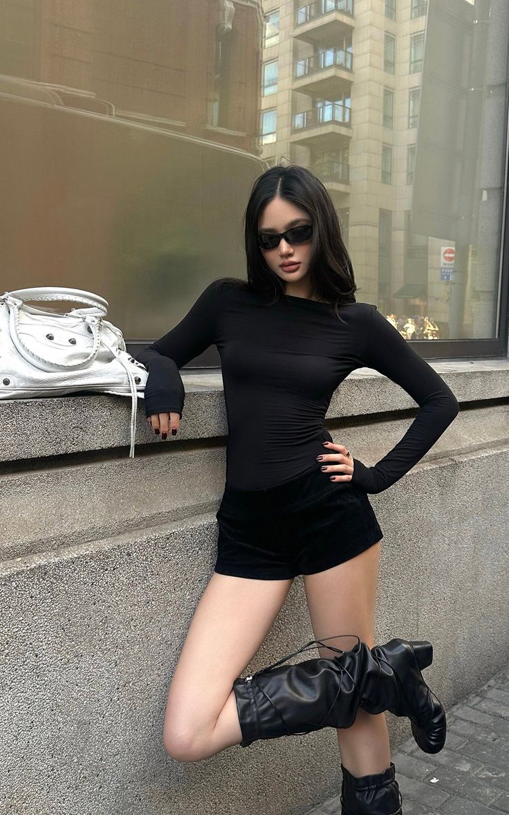 Woman in black top and shorts with sunglasses and a silver bag outdoors