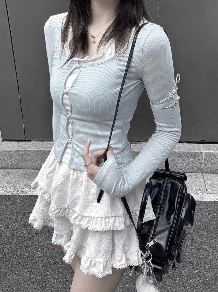 Person in a light blue long sleeve top and white ruffle skirt with a black shoulder bag