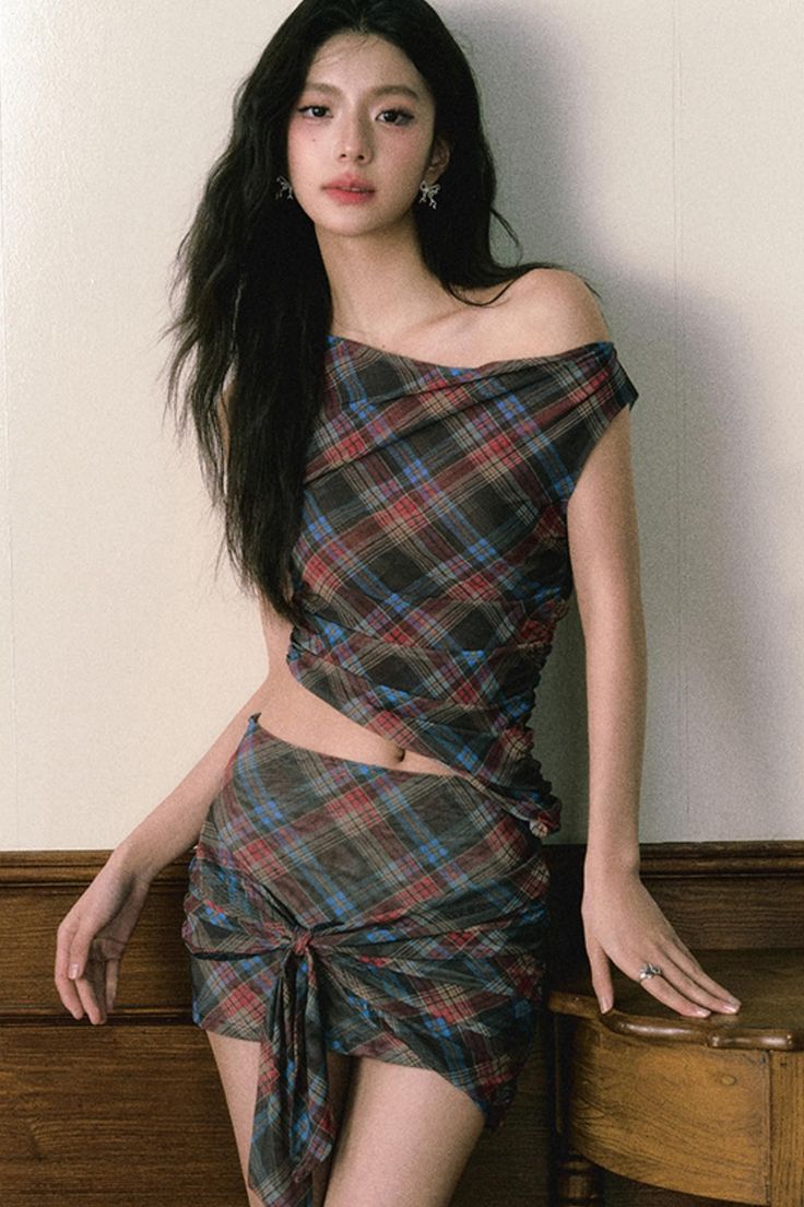 Woman with long dark hair wearing a plaid off-shoulder top and mini skirt