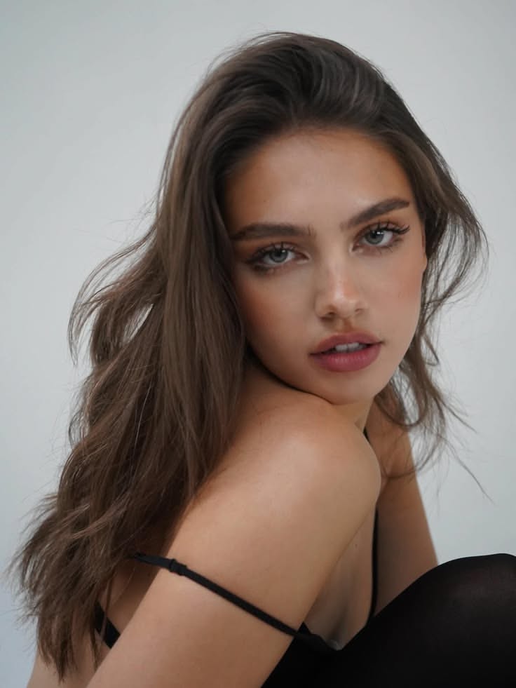Woman with long brown hair and a dropped strap looking over her shoulder