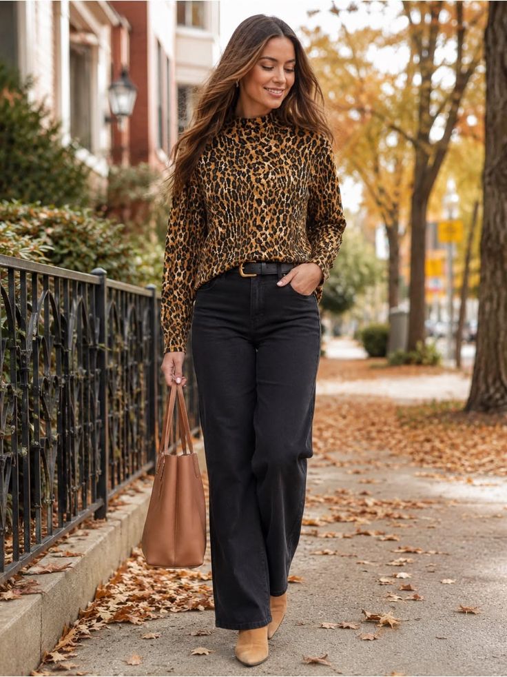 Woman in a leopard print top and black jeans walking on a street with autumn leaves