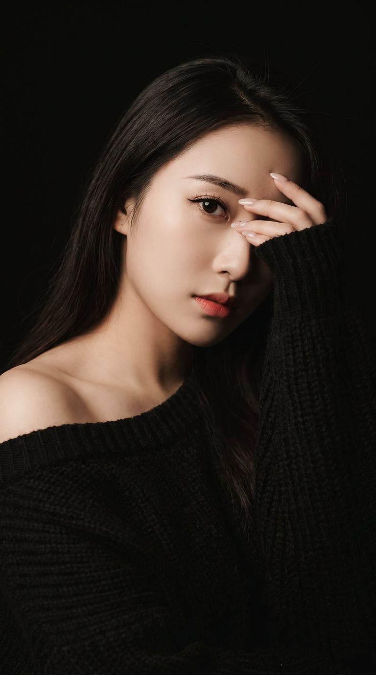 Woman with long black hair in an off-shoulder sweater on a dark background