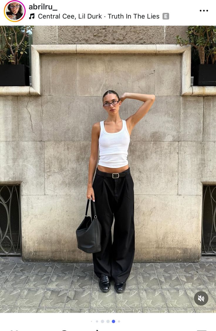 Woman in a white tank top and black wide-leg pants posing outdoors