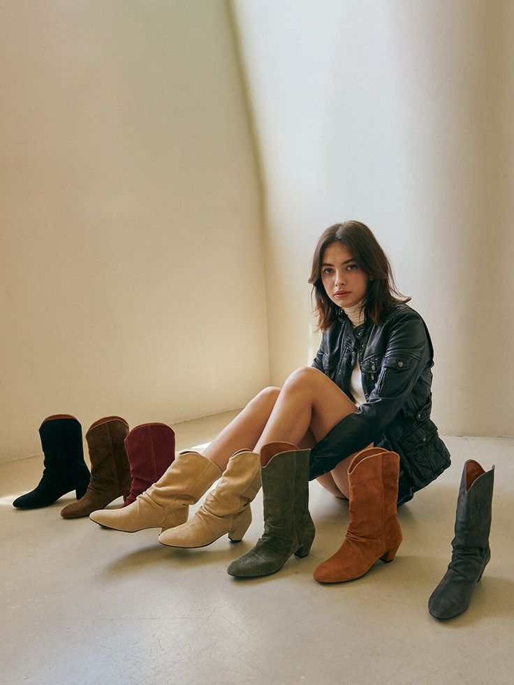 Woman in a leather jacket and short shorts sitting on the floor with cowboy boots
