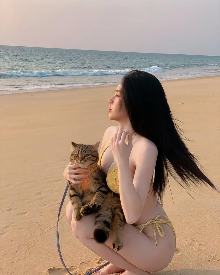 Woman in a yellow bikini holding a cat on a beach