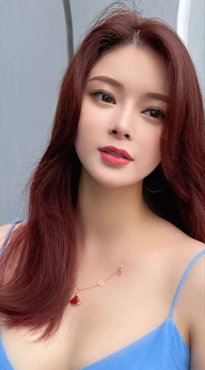 Woman with long red hair wearing a blue top and a necklace
