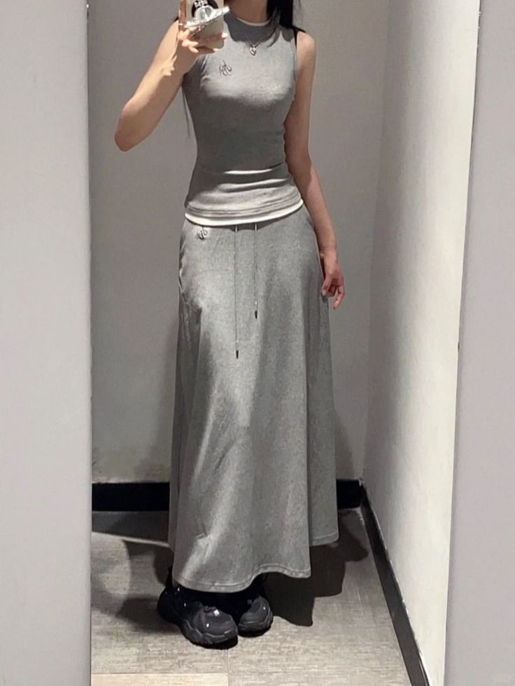Person in a gray sleeveless top and long skirt taking a mirror selfie