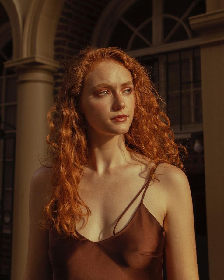 Woman with red curly hair and freckles in a brown top during golden hour