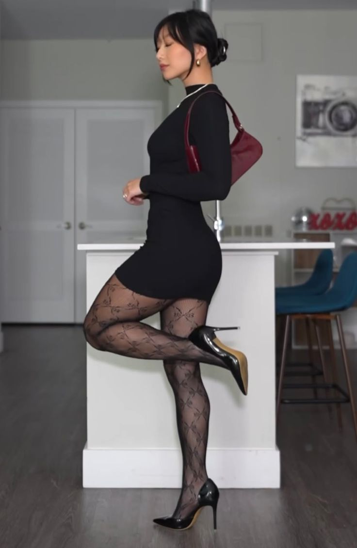 Woman in a black dress and patterned tights posing indoors