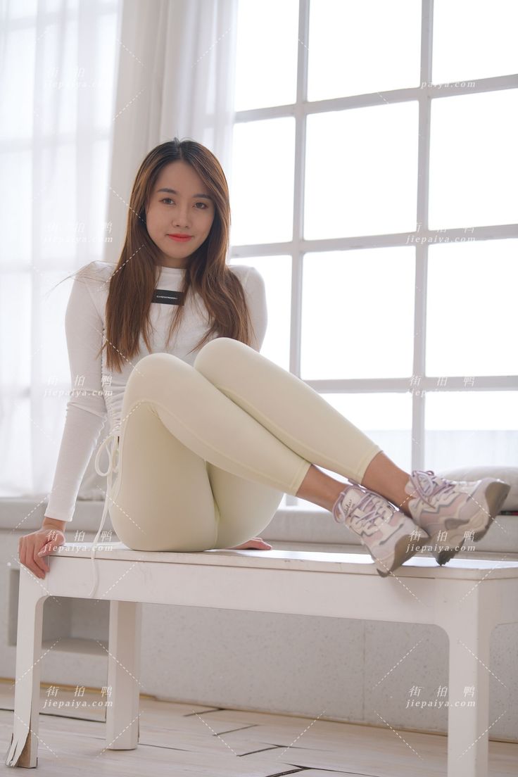 Woman with long hair wearing a white top and leggings, sitting indoors