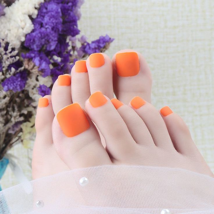 Feet with bright orange toenails, adorned with pearls and flowers