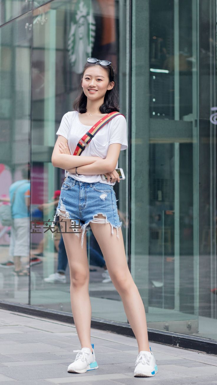 Woman in a white t-shirt and distressed denim shorts smiling on a street