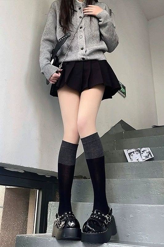 Person in a pleated skirt, cardigan, and knee-high socks on stairs