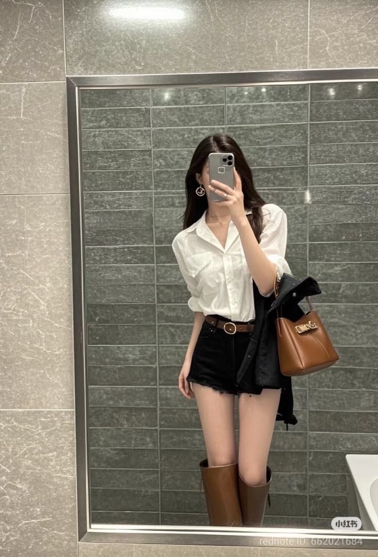 Woman in a white shirt and black shorts taking a mirror selfie