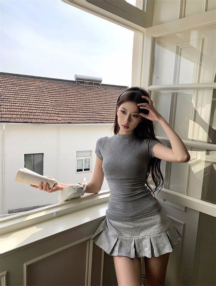 Woman in a grey dress and pleated skirt standing by a window