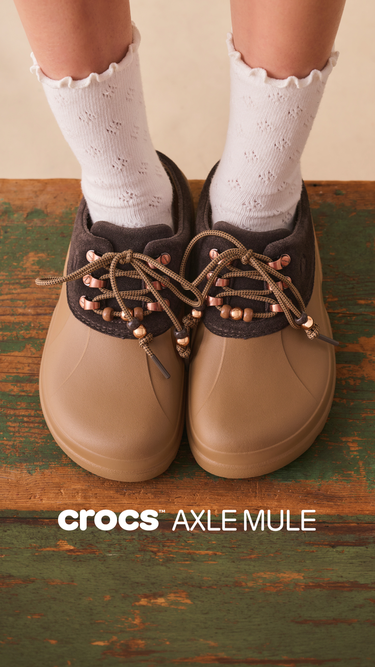 Pair of Crocs Axle Mule shoes with white ruffle socks on a rustic wooden surface
