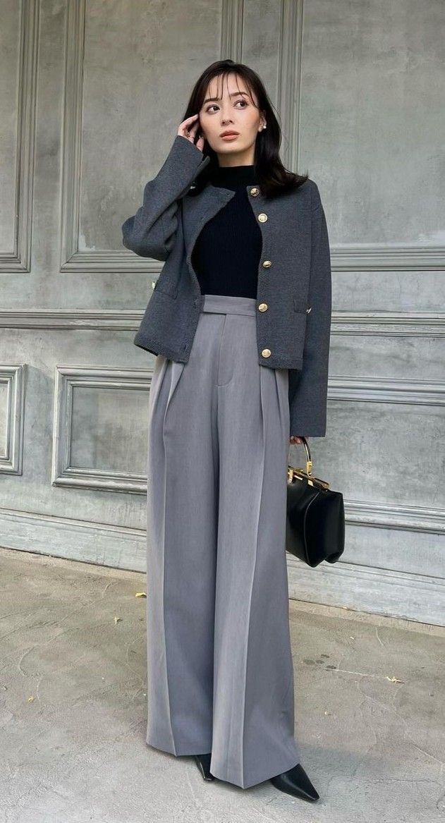 Woman in a gray jacket and wide-leg pants holding a black handbag