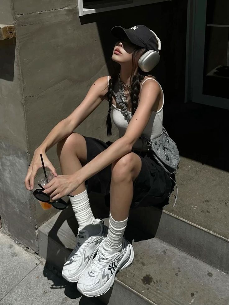 Woman with braids, cap, and headphones sitting outdoors