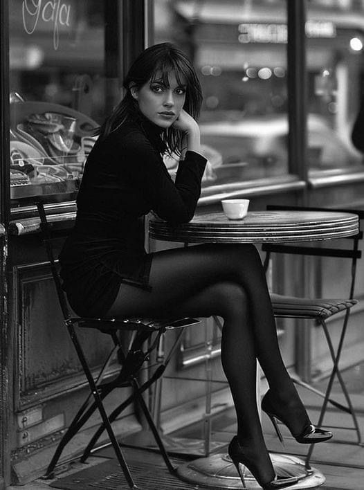 Woman in a black dress and tights sitting at an outdoor cafe table