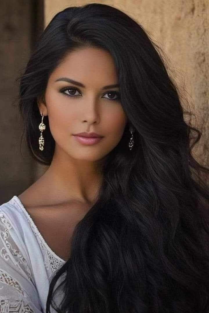 Woman with long black hair and earrings wearing a white top