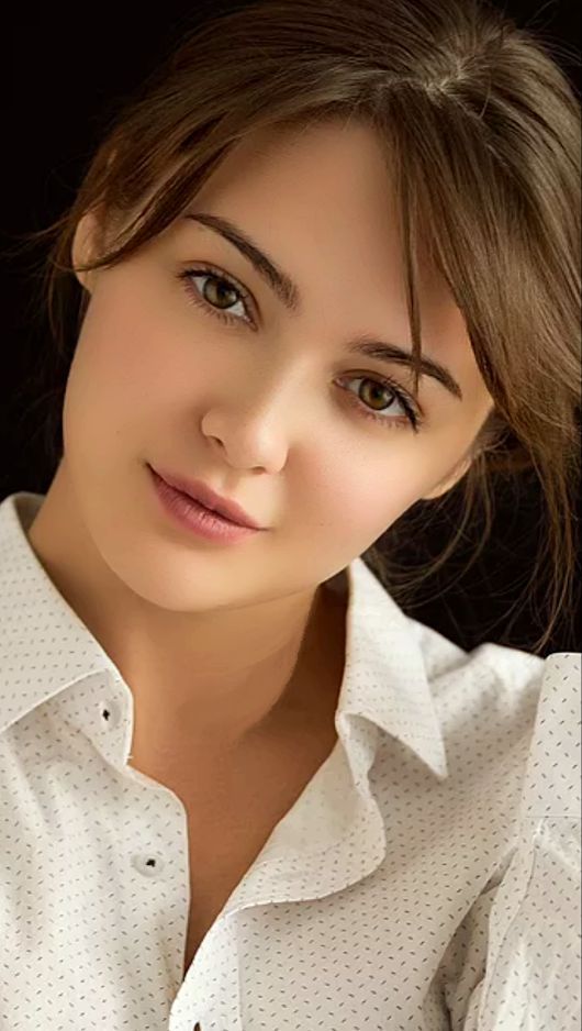 Woman with brown hair wearing a white shirt against a dark background