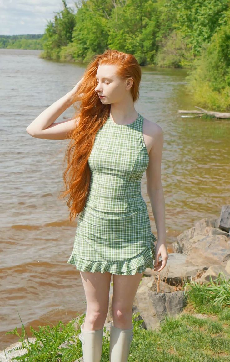 Woman with long red hair in a plaid dress standing by a river